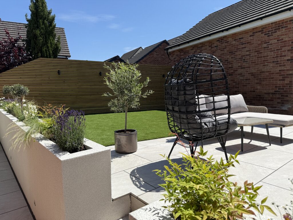 Modern garden with raised planters, olive trees, artificial lawn, porcelain paving and contemporary outdoor seating