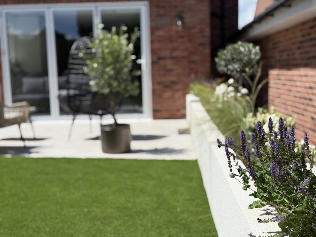 Lavender and mixed planting in a modern raised planter with artificial lawn and contemporary outdoor seating in the background.