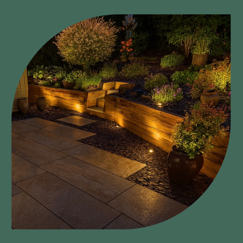 Warm garden lighting illuminating raised timber planters, planting beds and a porcelain patio at night