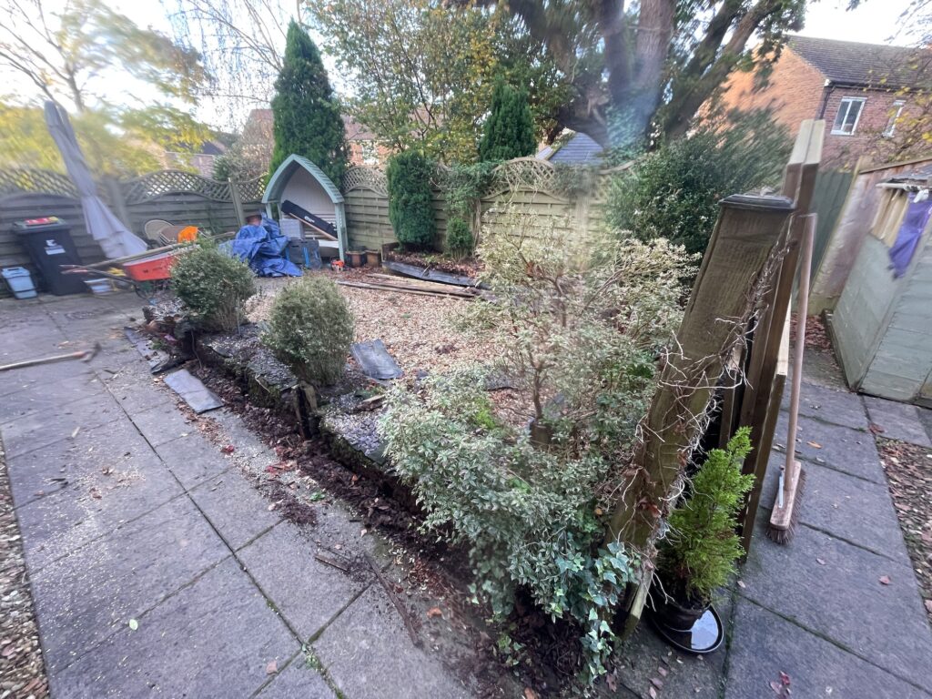 Before garden transformation showing overgrown shrubs, uneven raised beds and tired patio paving in residential garden