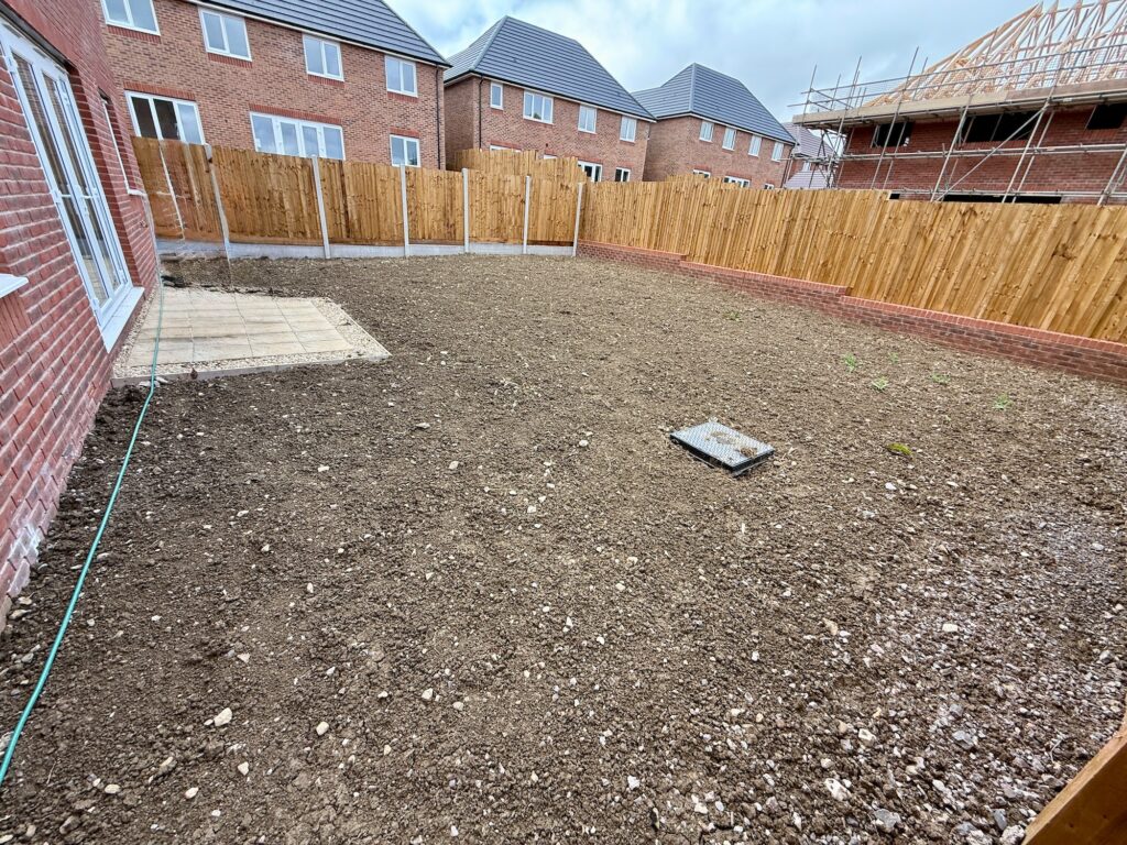 Bare new-build garden before landscaping with compacted soil and unfinished patio area