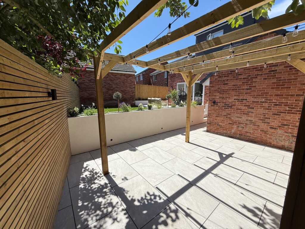 Timber pergola over porcelain paving in a modern landscaped garden with raised planters