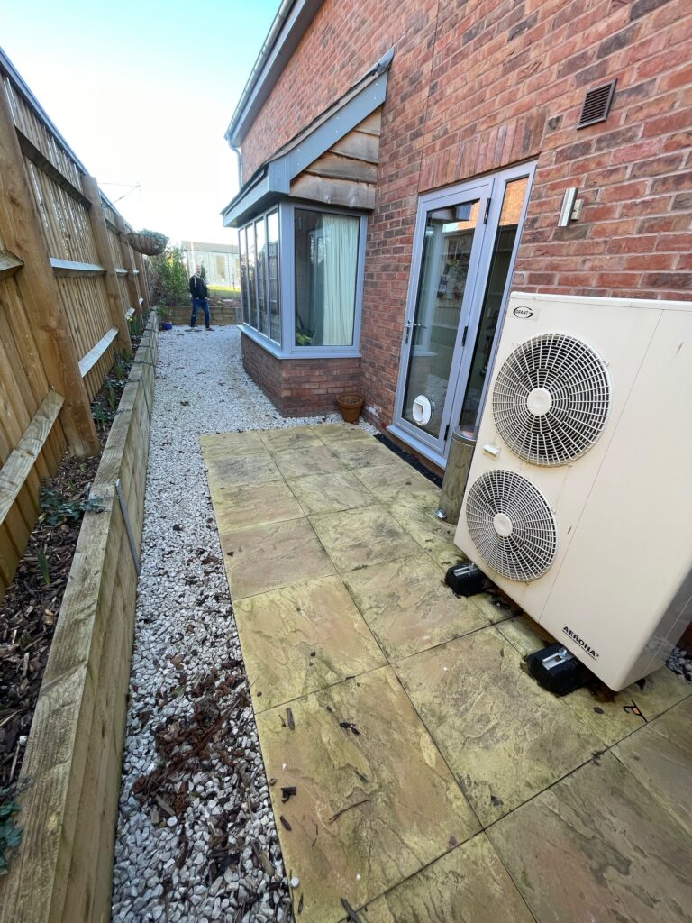 Porcelain paved utility area with gravel borders and air source heat pump installation beside a brick property