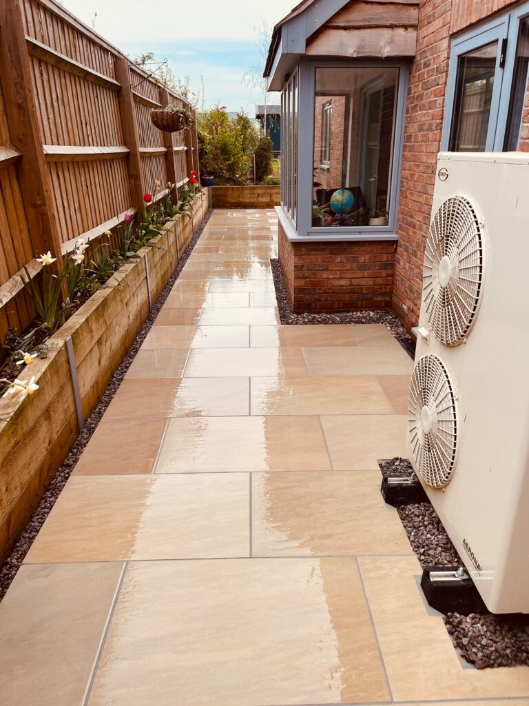 Porcelain paved side pathway with raised timber planters and gravel edging alongside a modern brick home