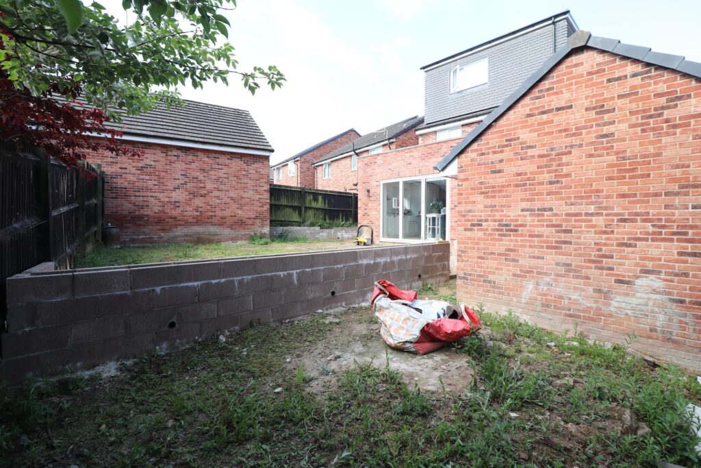 Garden before renovation with bare soil, block retaining wall and unfinished layout