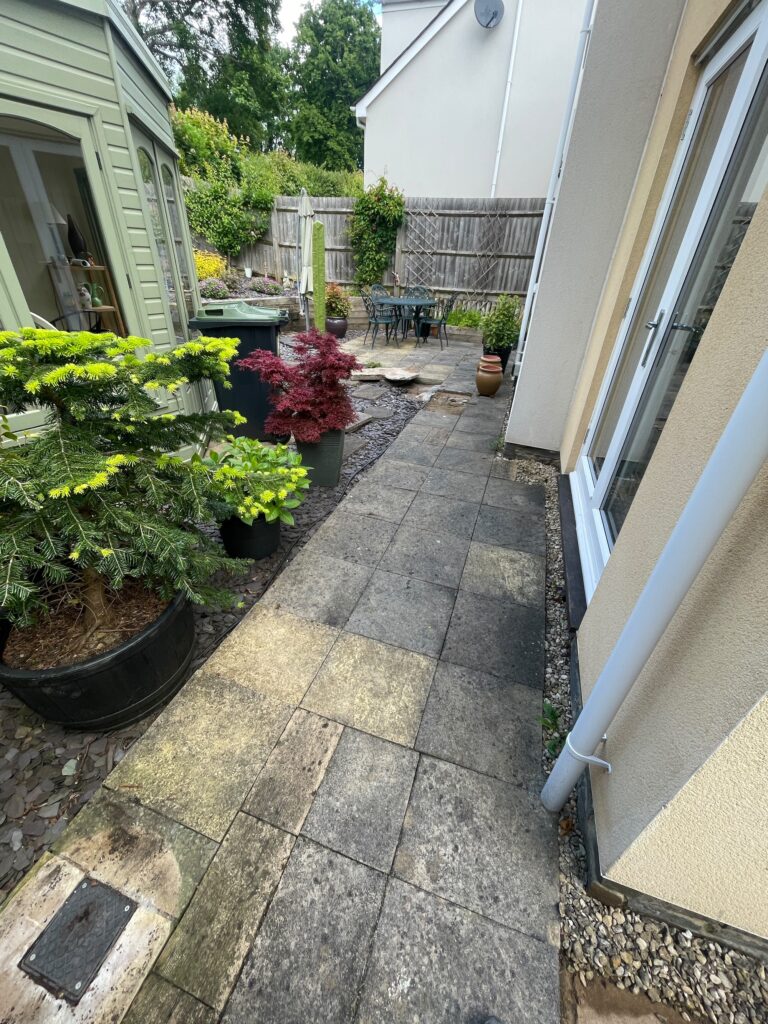 Before image of a narrow side garden with old paving slabs and uneven surfaces