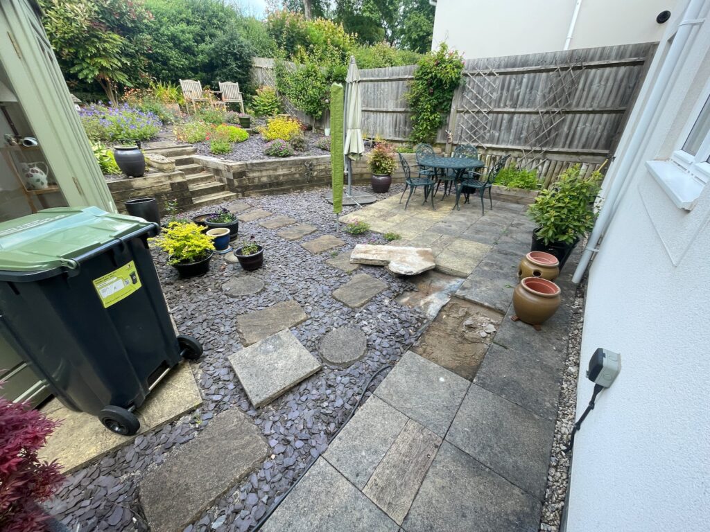 Before image of uneven garden with old paving slabs and gravel areas